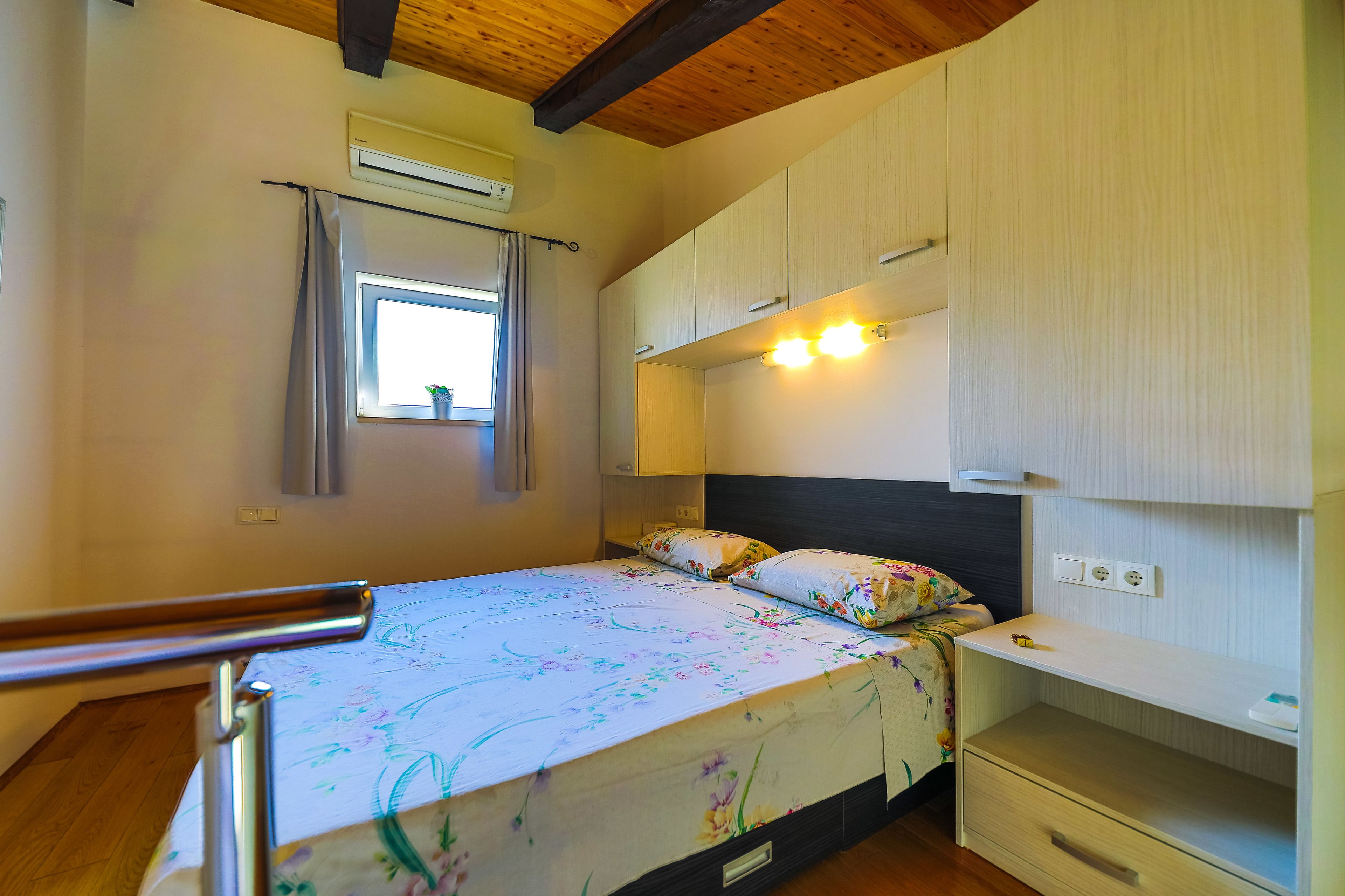 A bedroom with a bed, a window with curtains, a bedside table, and built-in cabinets.