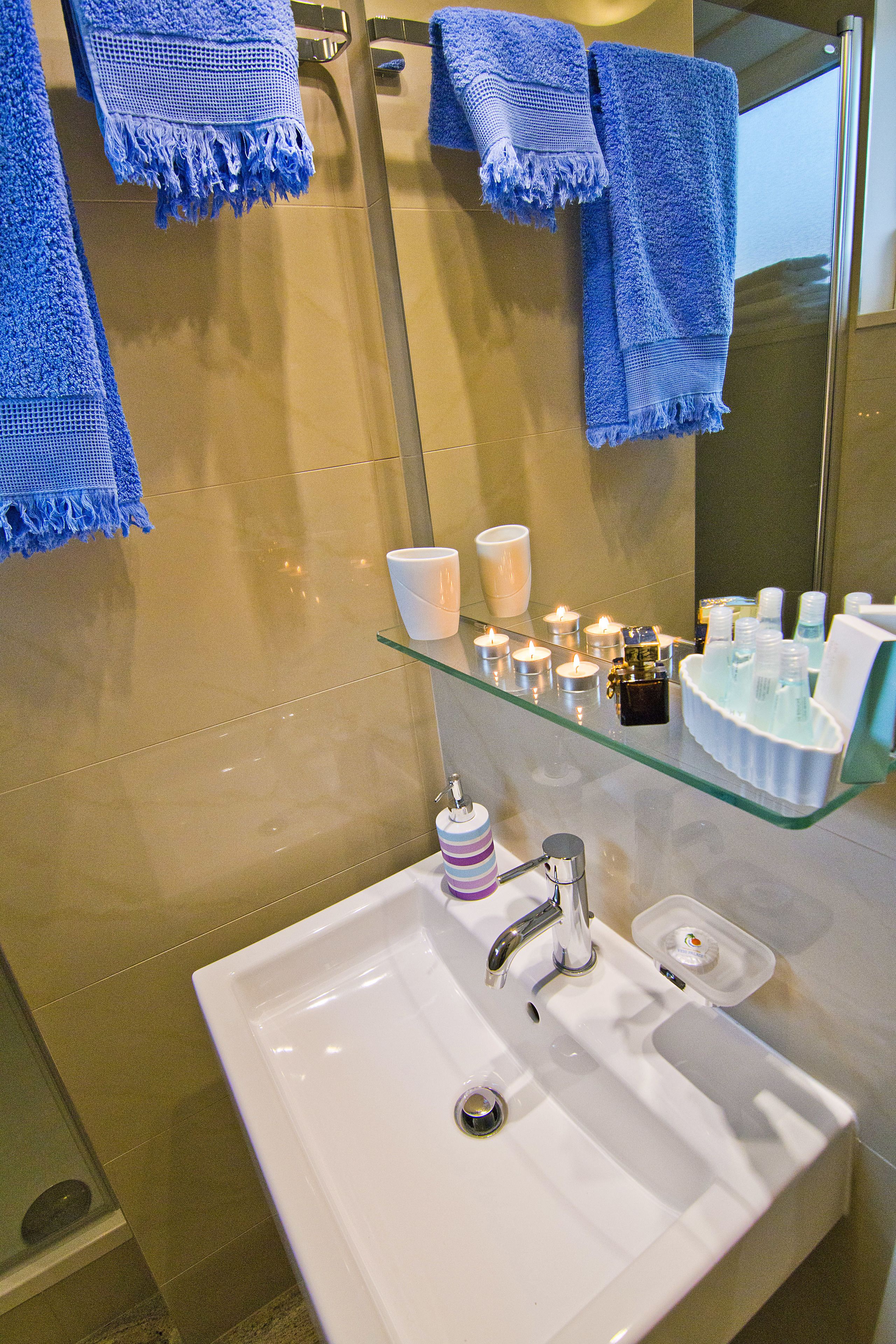 A bathroom with a white sink, a glass shelf with toiletries, and blue towels hanging on the wall.
