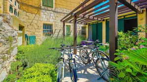 Um edifício de pedra com pérgola de madeira, bicicletas e vegetação exuberante.