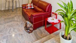 Um espaço de estar compacto com sofá de couro vermelho, uma pequena mesa de jantar, área de cozinha e um vaso com planta.