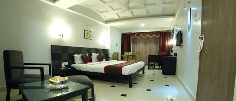 A hotel room with a bed, a desk, a chair, a table, and a TV.