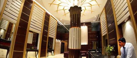 A hotel lobby with a central column, a reception desk, and a large chandelier.