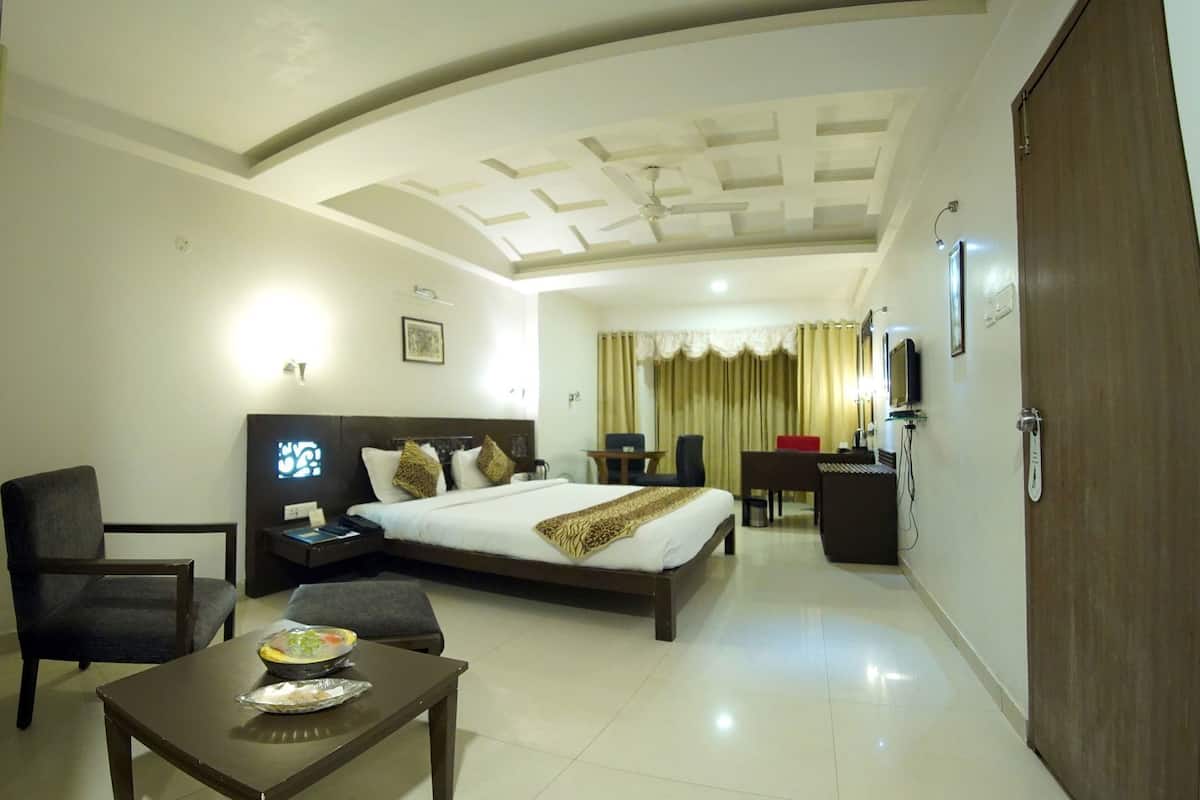 A hotel room with a bed, a desk, a chair, a small table with a bowl of food, a television, and a wardrobe.