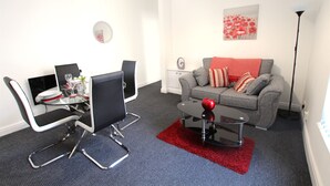 Ein modernes Wohnzimmer mit Essbereich, ein graues Sofa mit roten und weißen Kissen, ein roter Apfel auf einem schwarzen Couchtisch und ein roter Teppich.