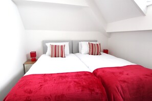 A double bed with red and white bedding, a gray headboard, and a red bedside table with a red lamp.