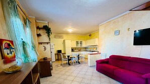 A living room with a red sofa, a wooden table with a glass bowl, and a kitchen area with white cabinets and a microwave. - Badualga Pink (San Teodoro)