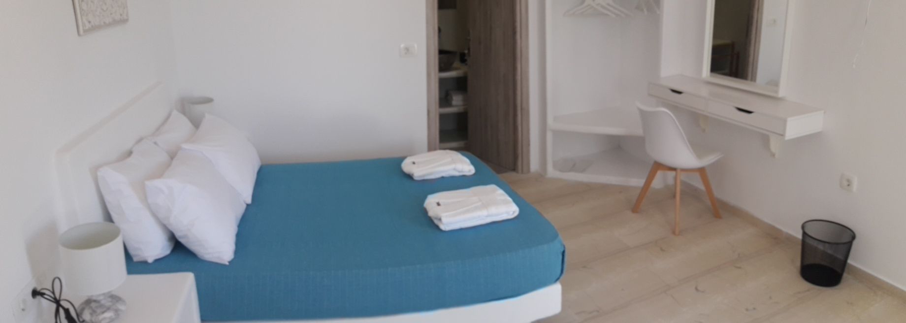A bedroom with a bed, pillows, a blue mattress, a white chair, a desk, and a small trash bin.