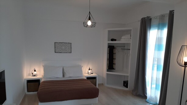 A bedroom with a bed, bedside lamps, a wardrobe, and a hanging light fixture. - Maistrali Prive (Santorini)