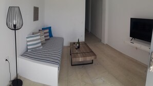 A modern living room with a sofa, a coffee table, a floor lamp, and a TV. - Maistrali Prive (Santorini)