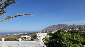 A coastal view with white buildings, a mountain in the background, and a clear blue sky. - Maistrali Prive (Santorini)