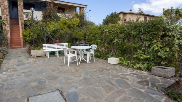 A stone patio with a table and chairs, surrounded by greenery and a stone wall. - Residence La Cinta 6 (San Teodoro)