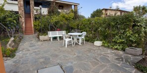 Relax on the patio surrounded by lush greenery, with a table and two chairs, and a bench for added seating.