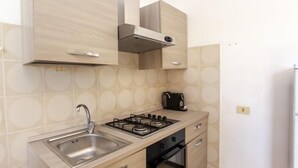 A compact kitchen with a stainless steel sink, a gas stove, and a black kettle. - Residence La Cinta 6 (San Teodoro)