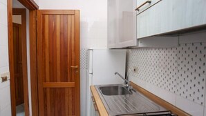 A small kitchen with a wooden door, white tiled walls, a stainless steel sink, and a patterned backsplash. - Residence La Cinta 2 (San Teodoro)