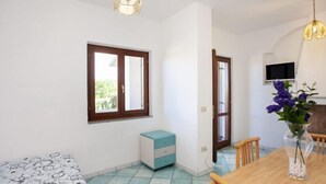A room with a bed, a small cabinet, a dining table with chairs, a vase with flowers, and a television on the wall. - Residence La Cinta 2 (San Teodoro)