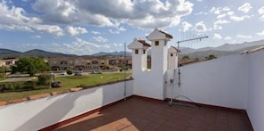 A rooftop terrace with a view of a residential area, including houses and mountains in the background.