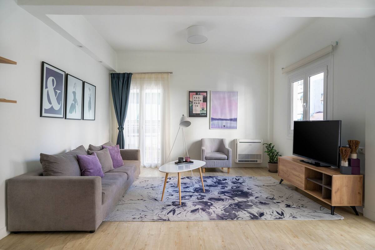 A modern living room with a sofa, a coffee table, a TV, and a large window.