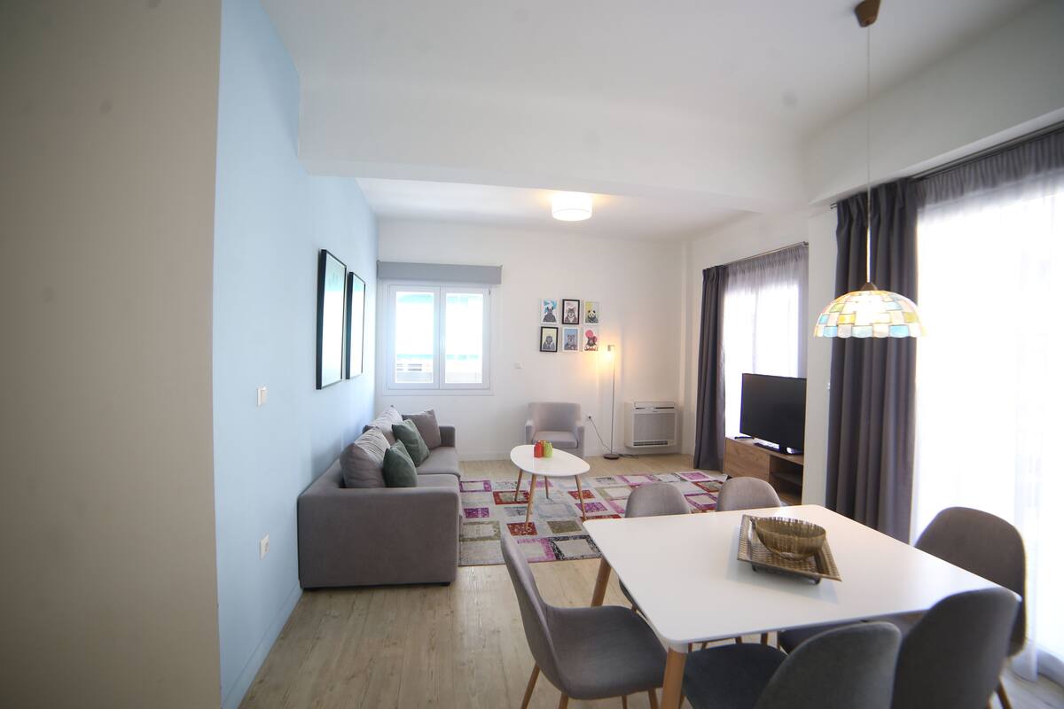 A living room with a sofa, a dining table with chairs, a TV, and a patterned rug.