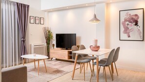 A modern living room with a dining area, a flat-screen TV, and a large abstract painting on the wall. - Athens Morum City Apartments (Vyronas)