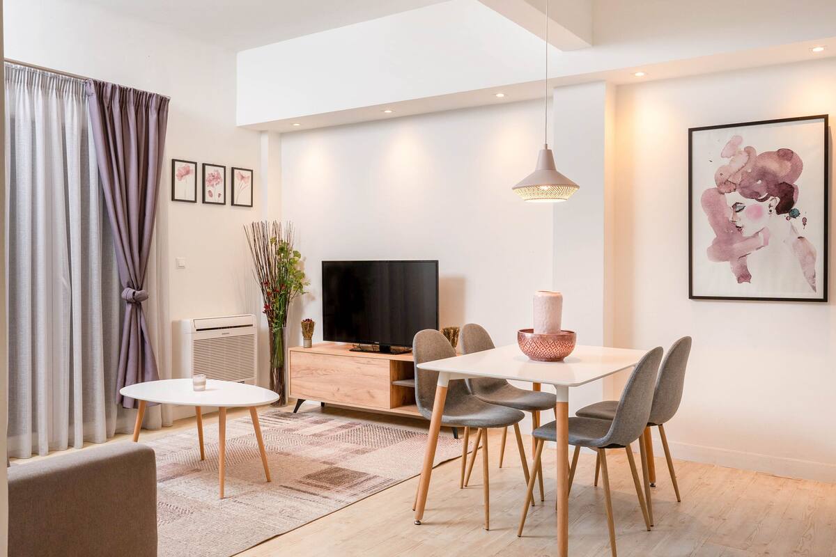 A modern living room with a dining area, a flat-screen TV, and a large abstract painting on the wall.
