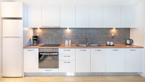 A modern kitchen with white cabinets, a built-in oven, a coffee maker, and a sink. - Athens Morum City Apartments (Vyronas)