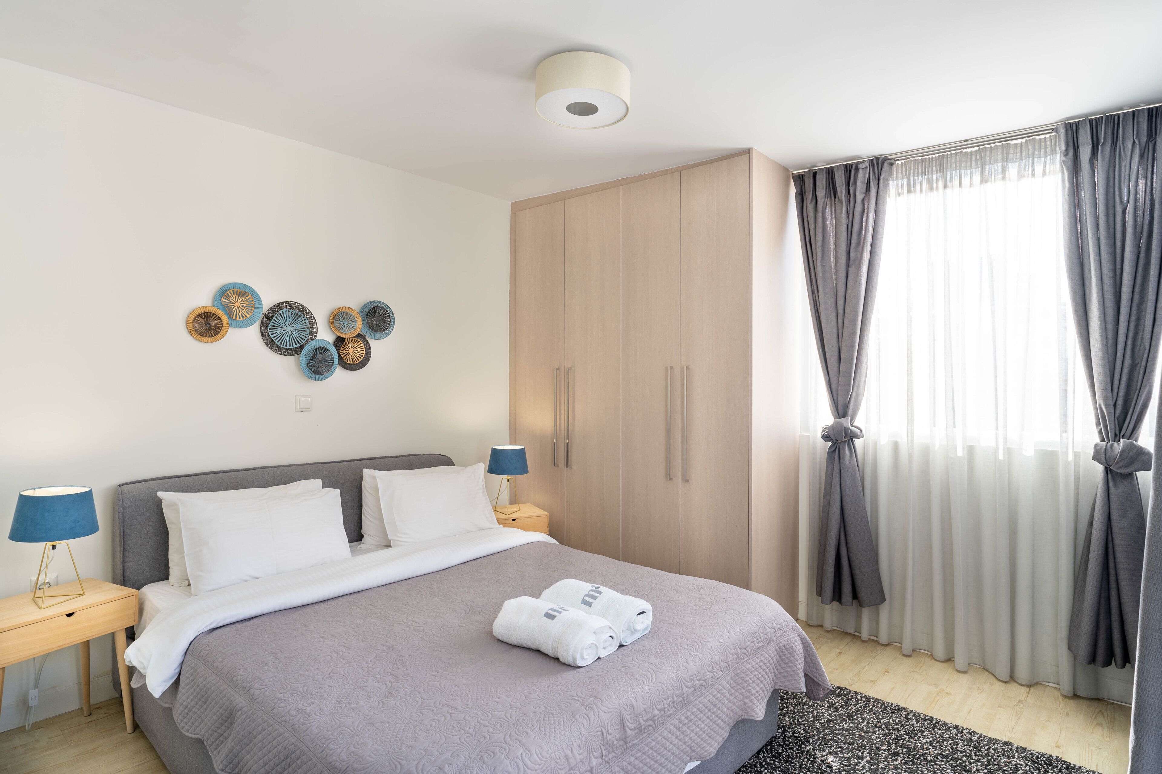 Une chambre bien rangée, avec un lit, des tables de chevet, une armoire et une fenêtre avec des rideaux.