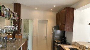 A modern kitchen with wooden cabinets, stainless steel appliances, and a glass-fronted bar area with bottles and glasses.