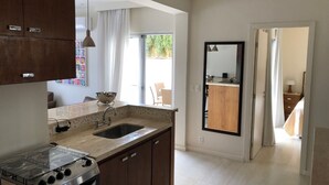 A modern kitchen with a gas stove, a sink, and wooden cabinets. There is a window with curtains, a mirror, and a view of the outside.