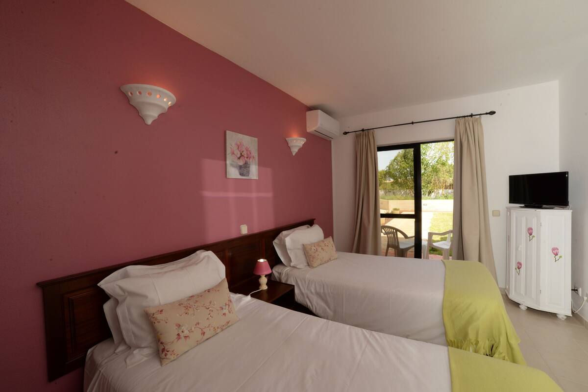 A hotel room with two beds, a TV, and a window with curtains.