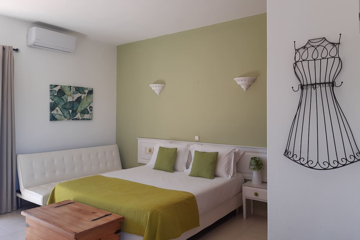 A bedroom with a bed, bedside tables, a wall-mounted air conditioner, a wall art piece, and a decorative wall piece.
