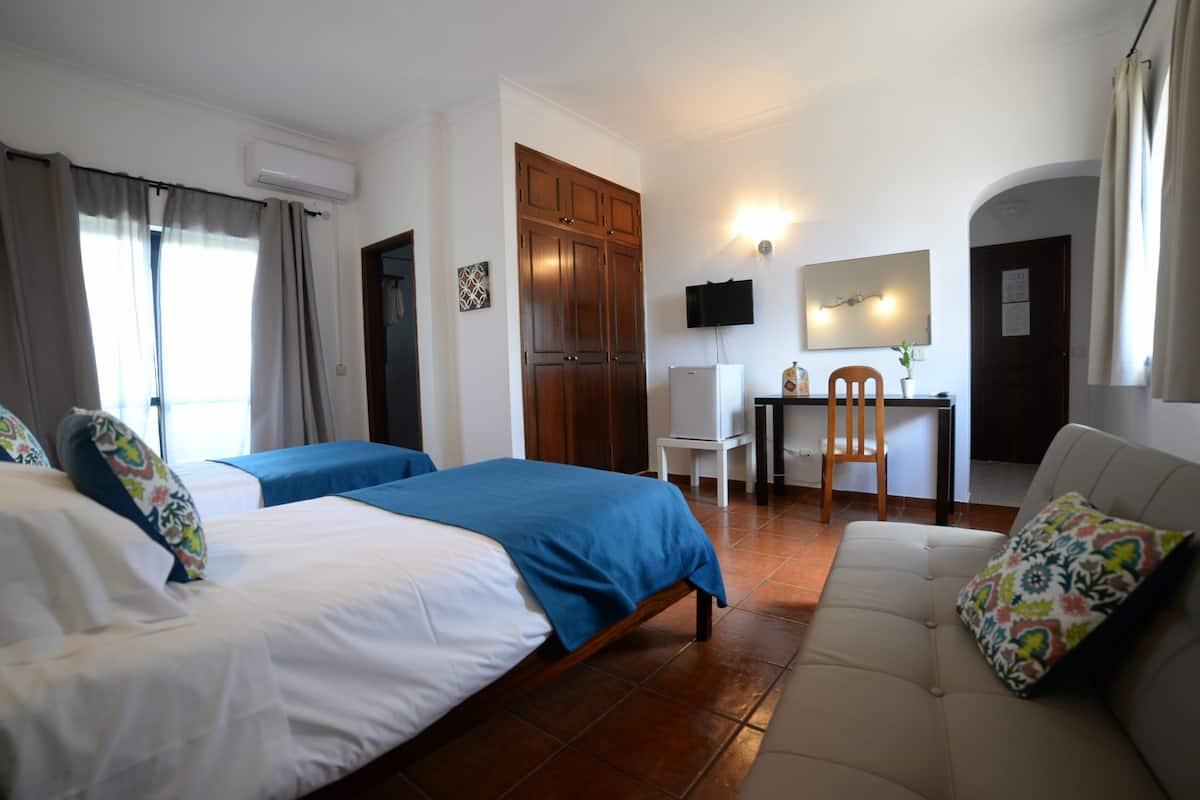 A hotel room with two beds, a sofa, a desk, and a TV.