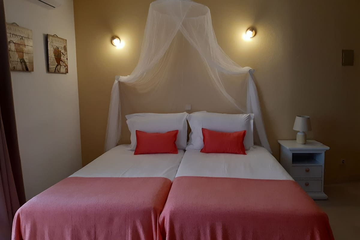 A room with a bed under a canopy, two bedside tables, and wall-mounted lights.