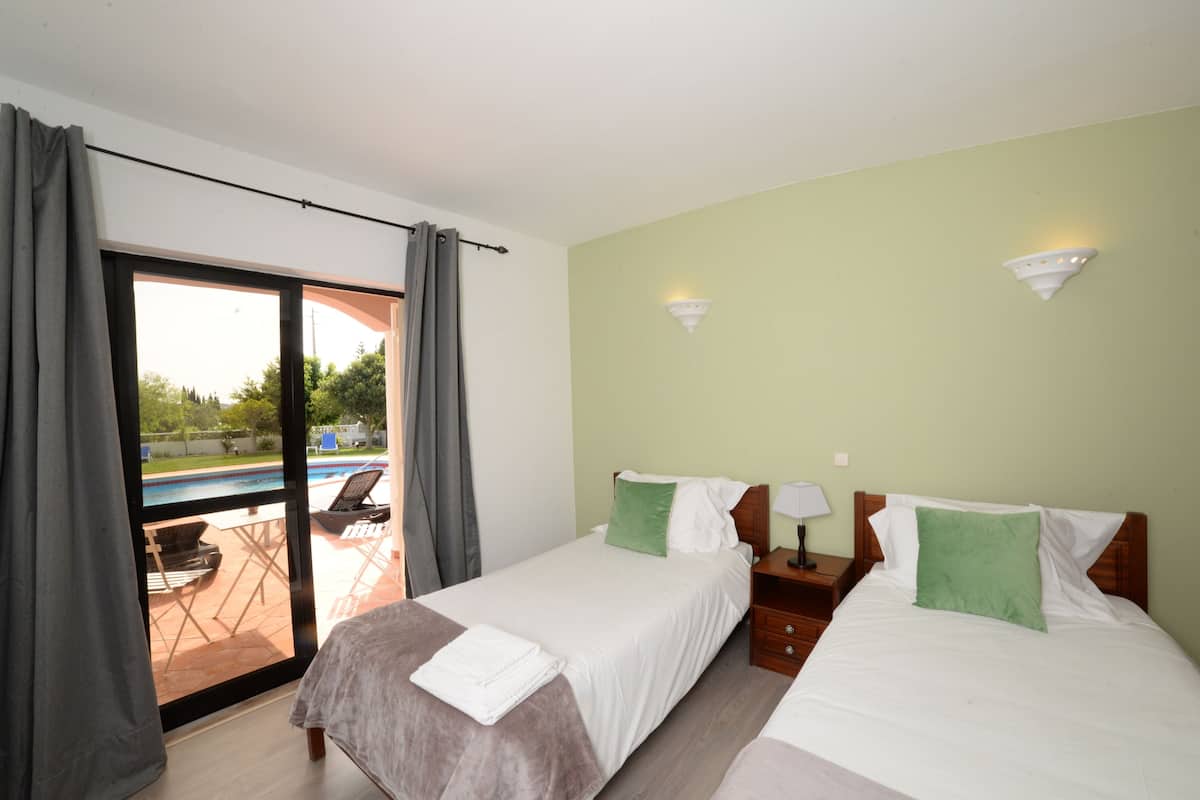 A hotel room with two beds, a sliding glass door to a pool area, and a green wall.