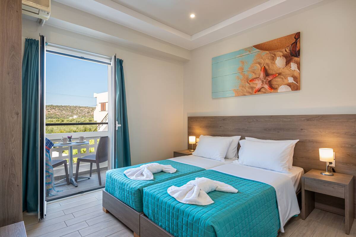 A hotel room with a balcony, a bed with two pillows, a nightstand with a lamp, and a painting on the wall.