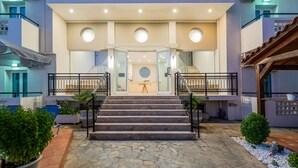A hotel entrance with a stone-paved pathway leading to a set of stairs, a glass door entrance, and a small garden area with potted plants. - Sisi Breeze Hotel (Agios Nikolaos)