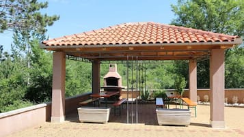 A covered outdoor area with a brick-tiled roof, a grill, and picnic tables.