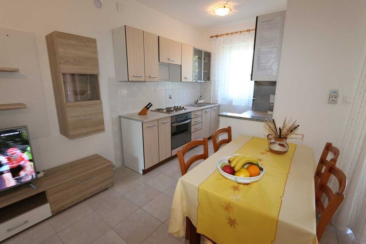 A compact kitchen with a dining area, a TV, and a fruit bowl on the table.