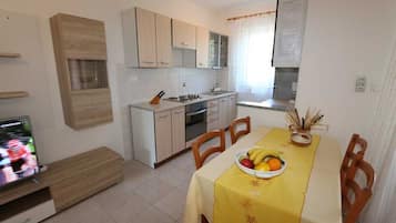 A compact kitchen with a dining area, a TV, and a fruit bowl on the table.