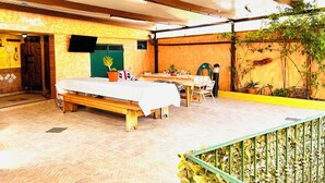 A room with a bed, a table, and chairs, a green door, and a wall with plants.