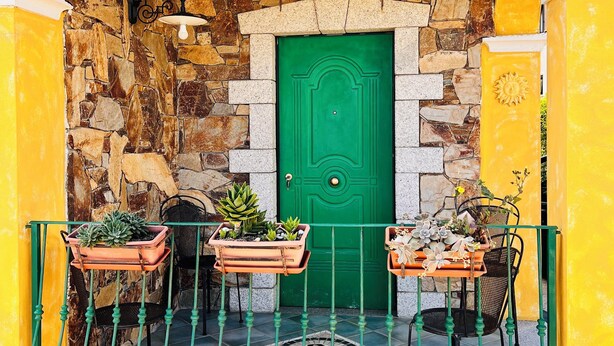 A yellow archway with a green door, potted plants, and a metal railing.