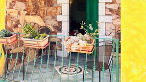 A stone facade with a green door, a metal railing, and potted plants.
