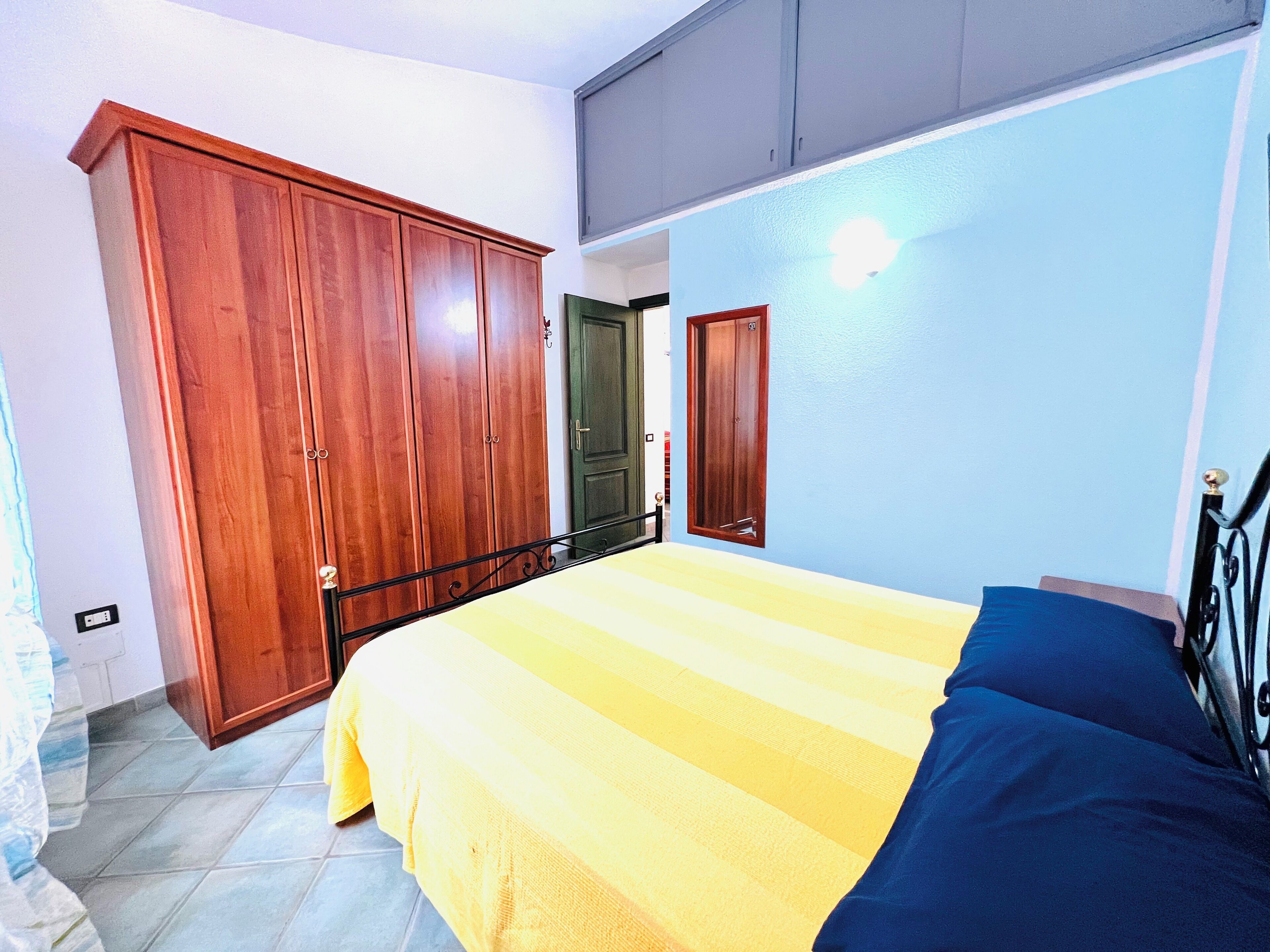 A bedroom with a bed, wooden wardrobe, and a door.
