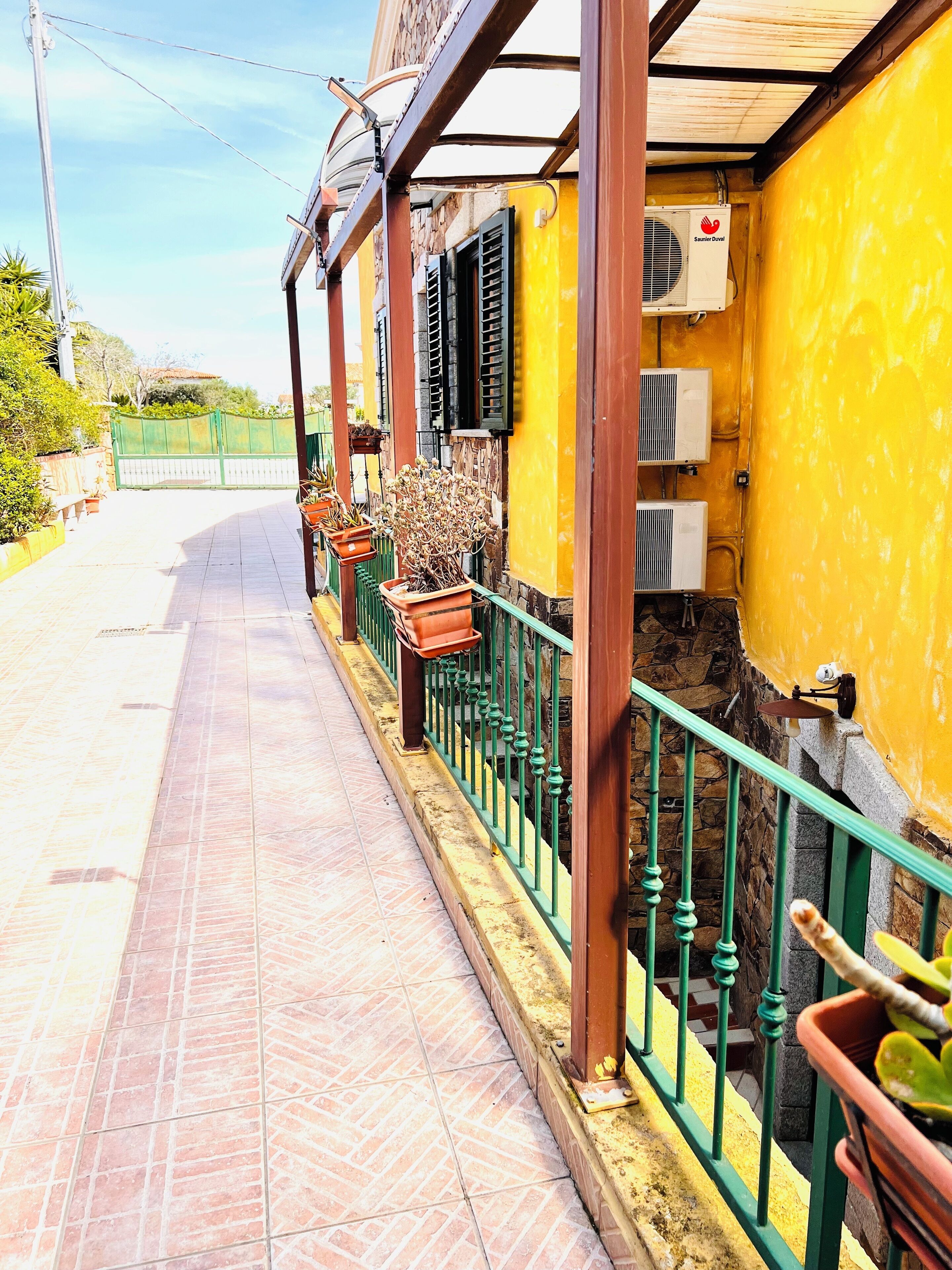 A covered outdoor area with a tiled floor, green metal railing, and potted plants.