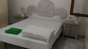 A neatly made bed with white linens, a green towel, and a decorative headboard. There are two bedside tables with lamps and a mirror on the wall. - Appartamenti San Teodoro VII (San Teodoro)