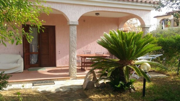 A covered outdoor seating area with a table and chairs, surrounded by stone pillars and a palm tree. - Appartamenti San Teodoro VII (San Teodoro)