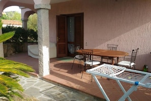 A patio with a round table and chairs, a white folding chair, and a door leading to a covered area.