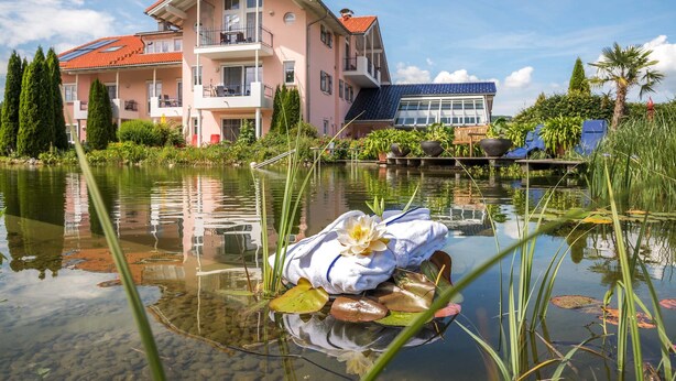 Een meerlaags gebouw met balkons, een vijver met waterlelies en een klein bootje met een bloem.