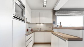 Una cocina moderna con armarios blancos, un microondas de acero inoxidable, un lavamanos y una ventana con vistas.