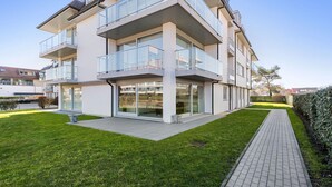 Un edificio residencial moderno de varios pisos, con balcones, ventanas grandes y un camino pavimentado.
