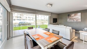 Una sala de estar moderna con comedor, ventanas amplias, un televisor de pantalla plana y un cuadro en la pared.